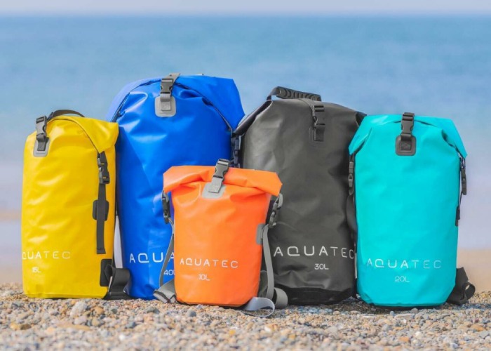  Some colorful dry bags each sit with a serene ocean and sky in the background.