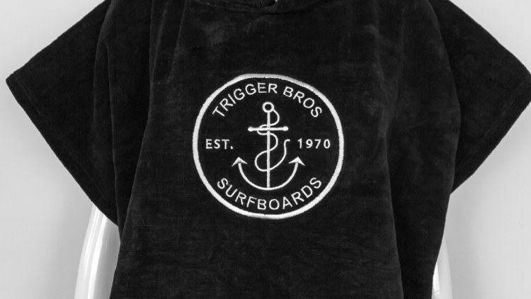 Black cotton surf poncho with white Trigger Bros Surfboards embroidery on chest