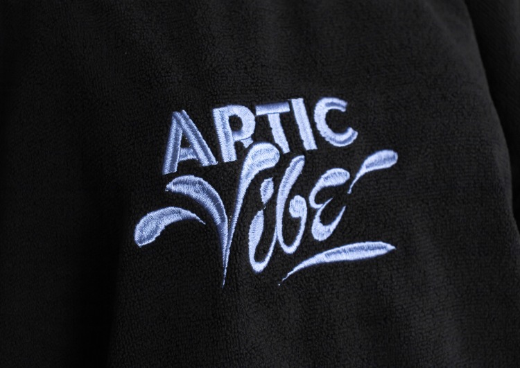 Close-up embroidery of ARTIC VIBE logo on black surf poncho.