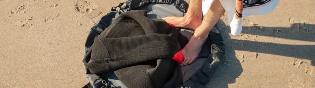 Person using a portable changing mat on the beach while changing clothes