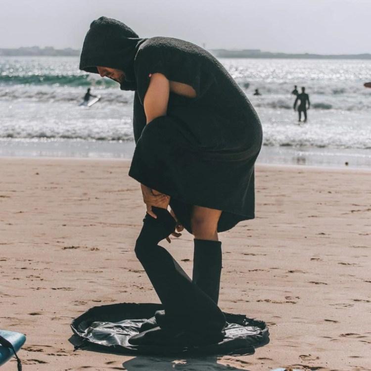 Man using surf changing mat on beach with wetsuit and poncho