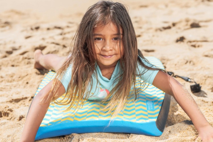 Young girl lying on bodyboard with attached leash on sandy beach
