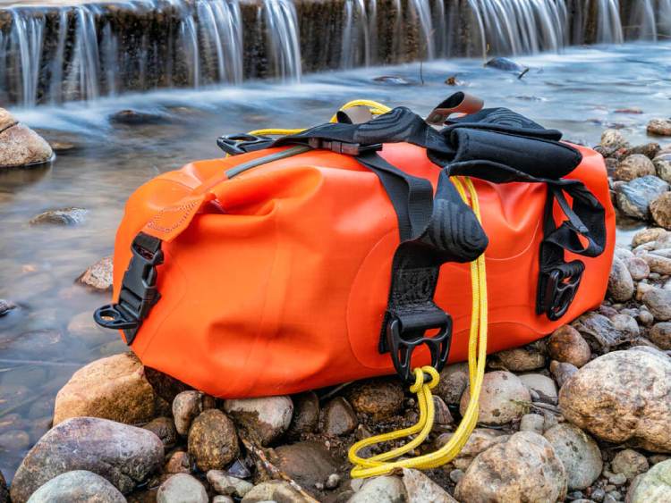 A Orange Duffel sitting by a river, fits for outdoor sports