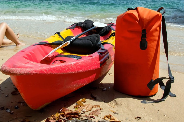 A Orange Waterproof Dry Bag Sitting with a Kayak 