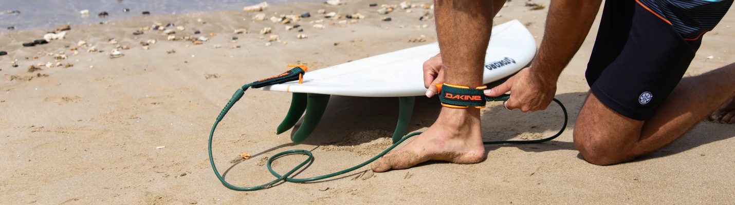 Surfer attaching a green surfboard leash to his ankle on the beach