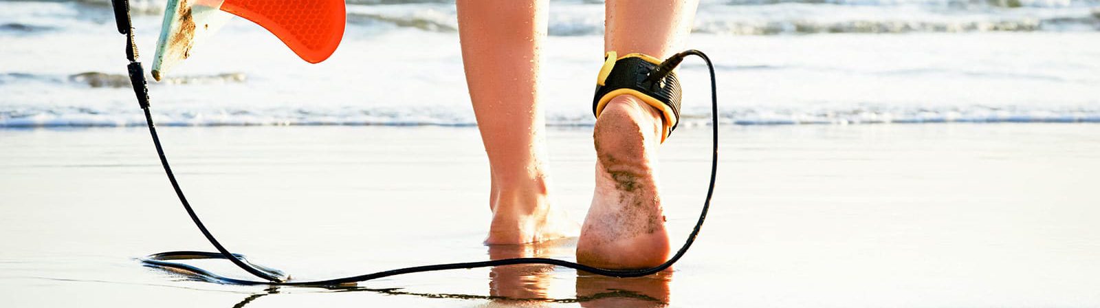 Close-up of surfboard ankle leash on beach with ocean reflection