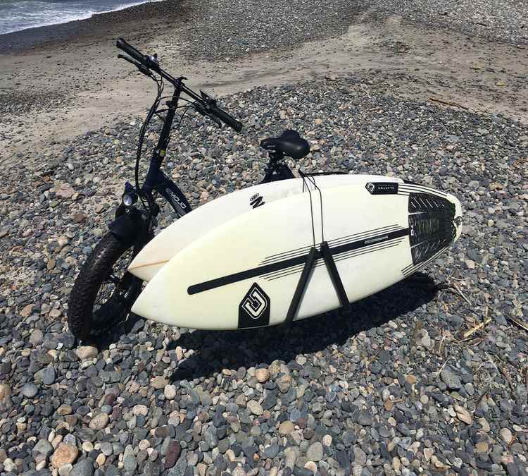Surfboard mounted on bike using side rack at the beach