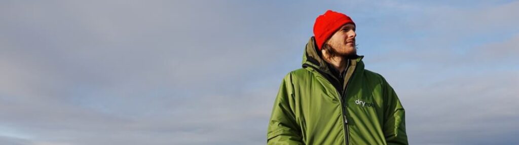 Surfer wearing a warm green changing robe with red beanie, ideal for post-surf warmth.