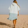 Back view of woman walking on beach in oversized two-tone surf changing poncho