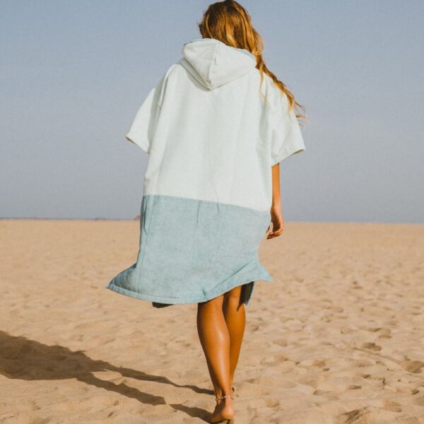 Back view of woman walking on beach in oversized two-tone surf changing poncho
