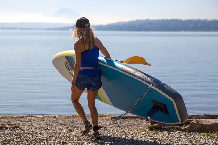 Woman walking by the lake with a stand up paddle board and coiled leash attached