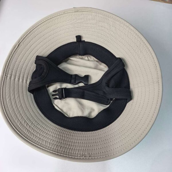 _cuva The image shows the inside of a surf fishing hat. The hat has a light beige color with a wide brim. The interior features a black adjustable strap with a plastic buckle, and a sweatband for comfort.