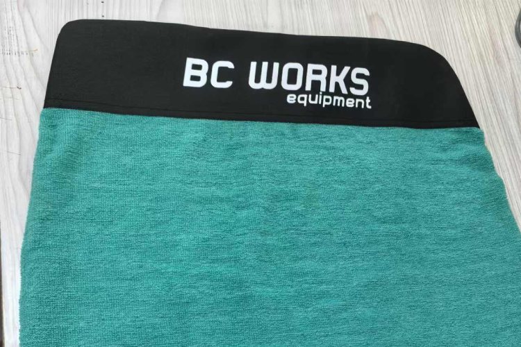  This surfboard sock features a teal body with a black top. The black top has the "BC WORKS equipment" logo printed in white.