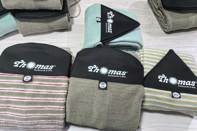 The image features several surfboard covers with the "Thomas" label, showcasing different colors and patterns.